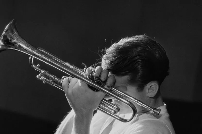 Chet Baker jouant de la trompette en noir et blanc, portrait de célébrité présenté dans l'exposition Fragile Beauté au Jeu de Paume