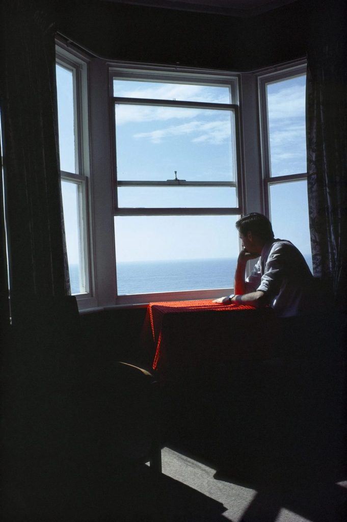 Homme accoudé à une fenêtre face à la mer à Brighton en 1979, photographie intimiste illustrant le thème de l'intime dans l'exposition Fragile Beauté au Jeu de Paume